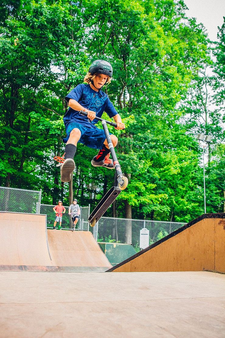 young person jumping a scooter at skate park